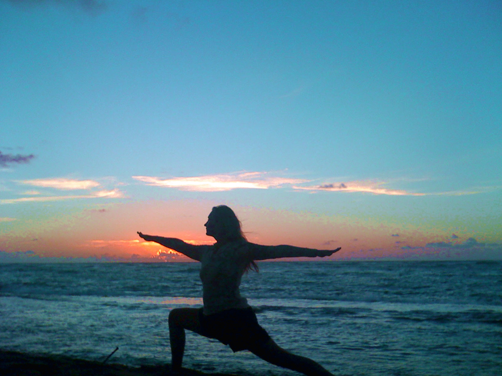 Person practicing yoga on a beach at sunRISE